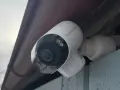 En vit Reolink Argus 4K övervakningskamera monterad under ett takutsprång.