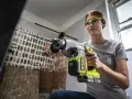 Kvinna med skyddsglasögon borrar i betongtak med en kraftfull slagborrmaskin. Damm virvlar upp från arbetet.