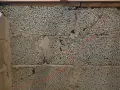 Synliga sprickor i grundmur av lättklinkerblock. En röd linje markerar en spricka som löper diagonalt över blocken.