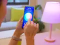 Person styr lampor med iPhone. Appen "Smart Home" visar färgval för vardagsrumsljuset.