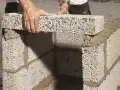 Händer lägger ett mura lecablock på en grund av cement. Byggnationen pågår utomhus.