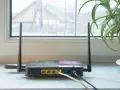 En gammal router med två antenner står på en fönsterbräda. En aloe vera-växt syns till höger.