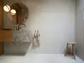 Modernt badrum med handfat i marmor och väggar av microcement. Enkel träpall och rund spegel.