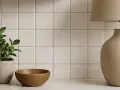 En krukväxt, en träskål och en lampa står framför en vägg med ljusa, fyrkantiga kakelplattor. En fin detalj som visar skillnad på kakel och klinker.
