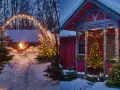 Varm julbelysning utomhus inspiration: snöiga stigar leder till en mysig eldstad och ett rött hus med julgranar.
