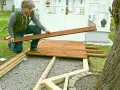 Man bygger trall vid ett växthus. Han håller en träbräda redo att läggas på plats.