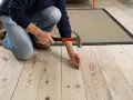 Man slår i en spik för att fixa ett knarrande golv av träplankor.