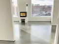 Ett modernt vardagsrum med en öppen spis och stora fönster som vetter mot en snötäckt trädgård. Golvet är ett vackert polerat betonggolv som reflekterar ljuset.