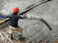 Arbetare med röd hjälm gjuter betong med en pump.