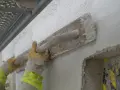 Händerna i gula handskar drar en träslev över en vägg, applicerar putsbruk b eller c för att skapa en jämn yta.