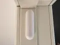 En vit, avlång sensor med en knapp sitter monterad på en ljusbeige dörrkarm. Den är en del av ett Aqara Thread-system för smart hem.