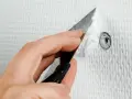 Hand spacklar ett litet hål i en vit, strukturerad vägg med en spackelspade.