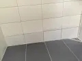 Fuktskada kakel i duschen. Mörka fläckar syns på de ljusa väggplattorna, ett tecken på fuktproblem.