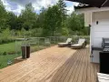 Solig altan med olja trall, solstolar och grill. Vacker utsikt över grönskande skog.