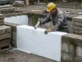 Bygger grund med isolering av cellplast. En man med gul hjälm applicerar fogskum för att fästa isoleringen.