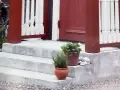 Nygjuten betongtrappa med röda stolpar och vita baluster. Krukor med växter och stenar pryder trappsteget.