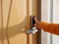 En hand med orange tröja använder fingeravtrycksläsaren på ett modernt dörrlås. Kanske ett nimly touch pro problem uppstod?