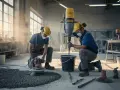 Två byggarbetare förbereder sig för att gjuta betonggolv. En blandar cement i en hink med en kraftig blandare, medan den andra förbereder ytan med en polermaskin.