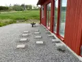 Stigande steg av altan plintar eller plattor leder genom grusgången fram till ett rött hus med stora fönster.