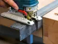 En hand använder en sticksåg för att såga snett i en metallprofil.