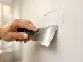 Hand med spackelspade breddar spackel på en vägg. Torktid spackel är viktig för ett jämnt resultat.