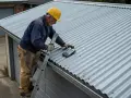 Man på stege mäter lutningen på ett plåttak. Instrumentet visar 4,5 grader, vilket är en bra minsta lutning för plåttak.