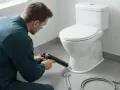 Hantverkare använder fogpistol för att limma toalettstol. Verktyg som skiftnyckel och slang ligger redo.