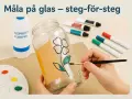 En hand målar ett blommönster på ett glas med en pensel. Färger, alkohol och andra tillbehör för att måla på glas ligger bredvid.