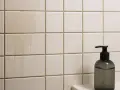 Smutsiga kakelplattor med rinnande vattenfläckar. En mörk tvålbehållare står till höger. Dags att ta bort kakel och rengöra.