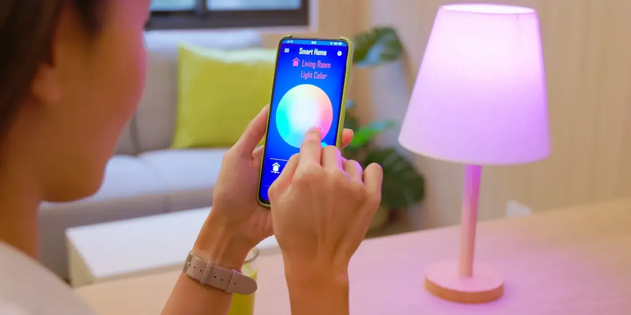 Person styr lampor med iPhone. Appen "Smart Home" visar färgval för vardagsrumsljuset.
