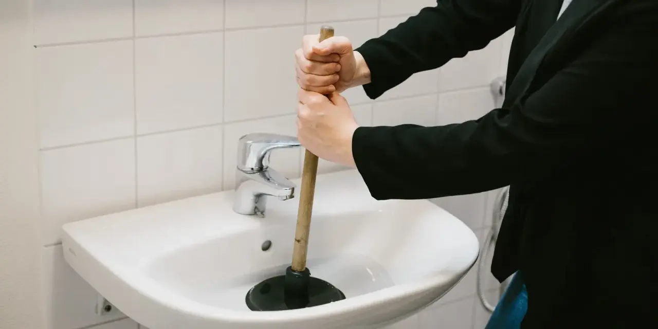 Person använder en sugpropp för att rensa vattenlås i handfatet.