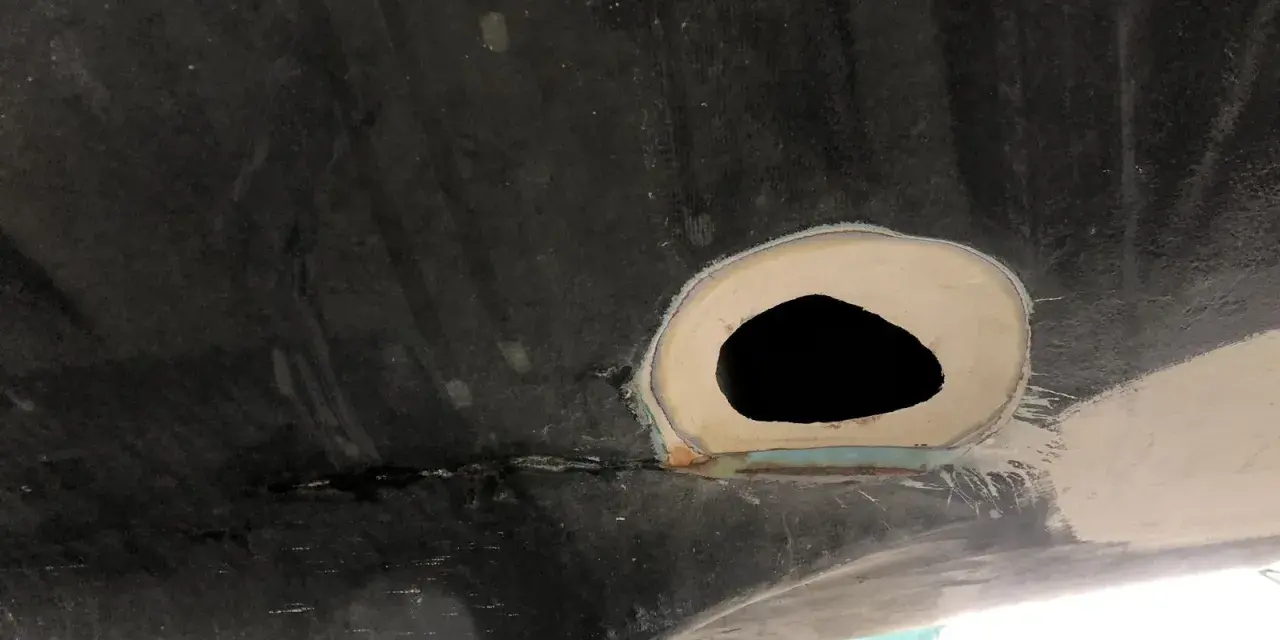 Förberedelse för att laga glasfiber. Ett hål i en mörk yta, omgivet av spackel och slipat material.