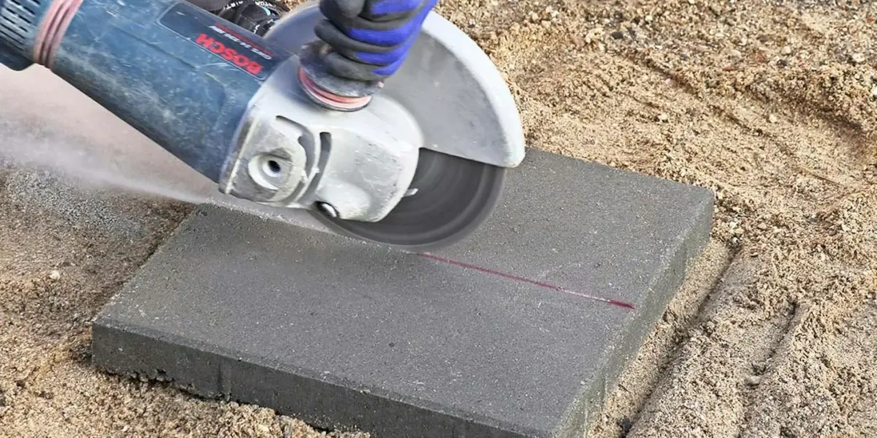 En person kapar marksten med en vinkelslip. Damm virvlar upp när stenen delas längs en markerad linje.