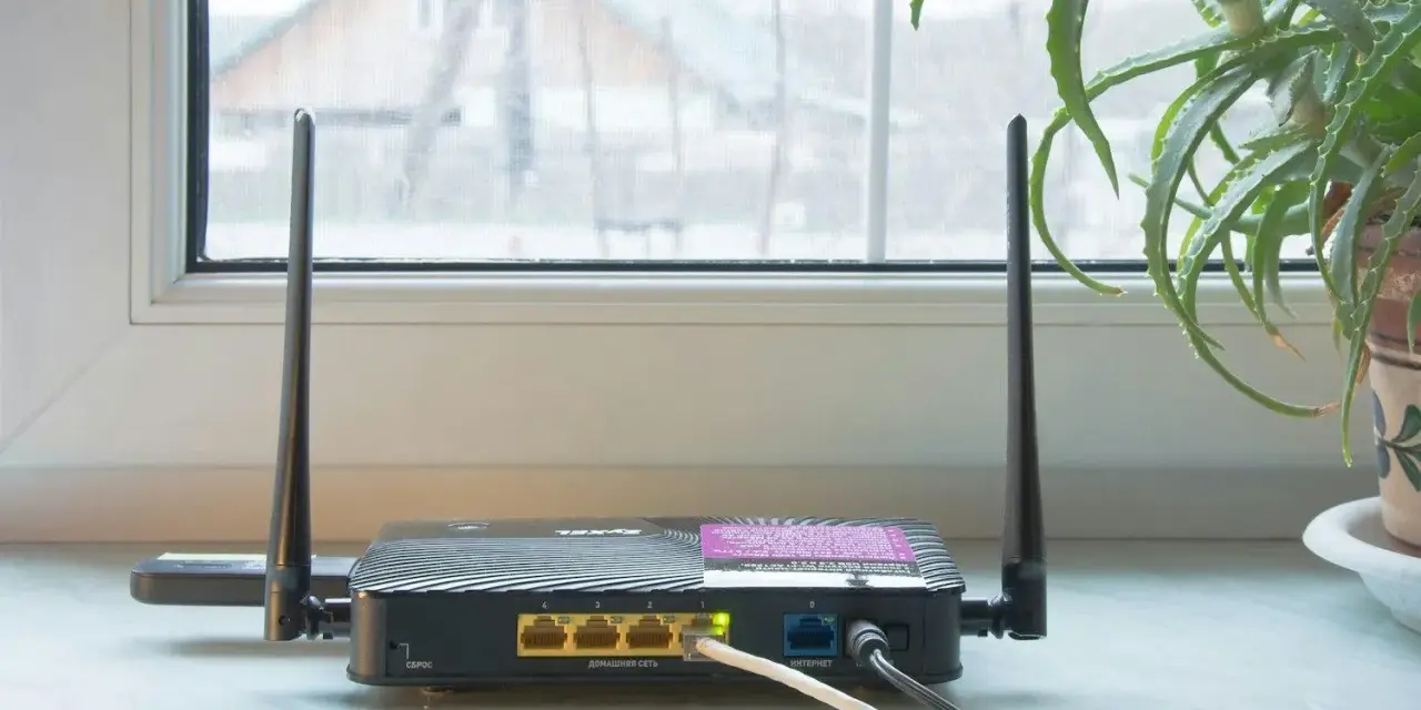 En gammal router med två antenner står på en fönsterbräda. En aloe vera-växt syns till höger.