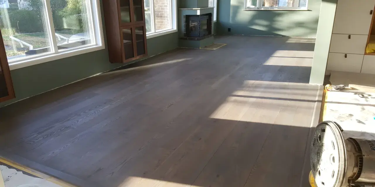 Ett rum med nylagt hårdvaxoljat golv. Solen lyser in genom fönstren och skapar vackra skuggor på det grå trägolvet.