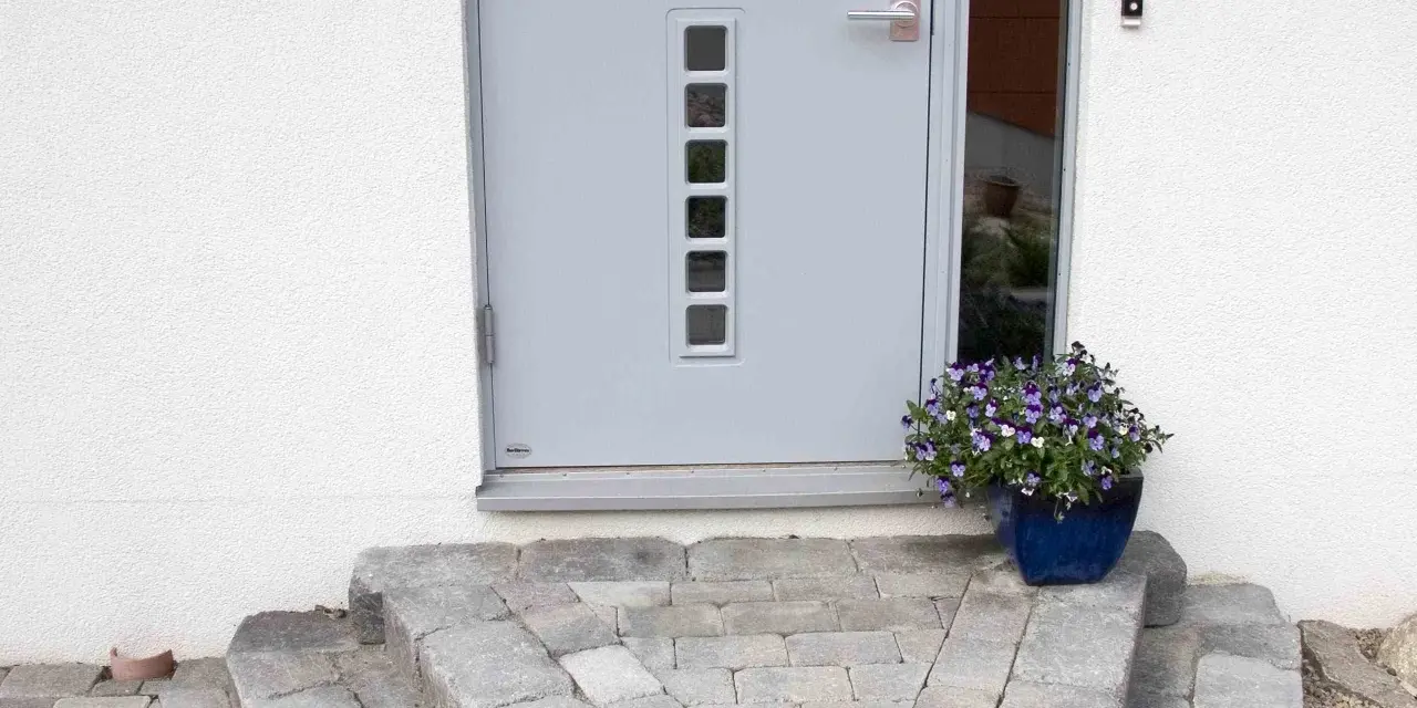 En vacker stentrappa leder upp till en modern ytterdörr. En blå kruka med blommor ger färg åt entrén.