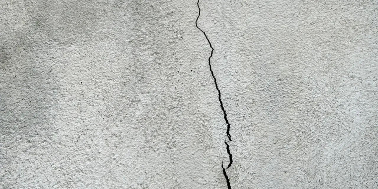 Spricka i en grå, putsad fasad. Dags att laga putsad fasad för att förhindra större skador.