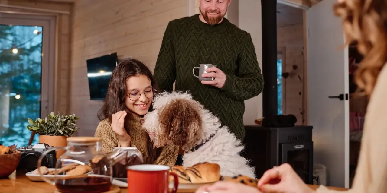 Familj med hund myser vid bordet med fika. Trots att det är lite dålig luft hemma, sprider sig värme och glädje.