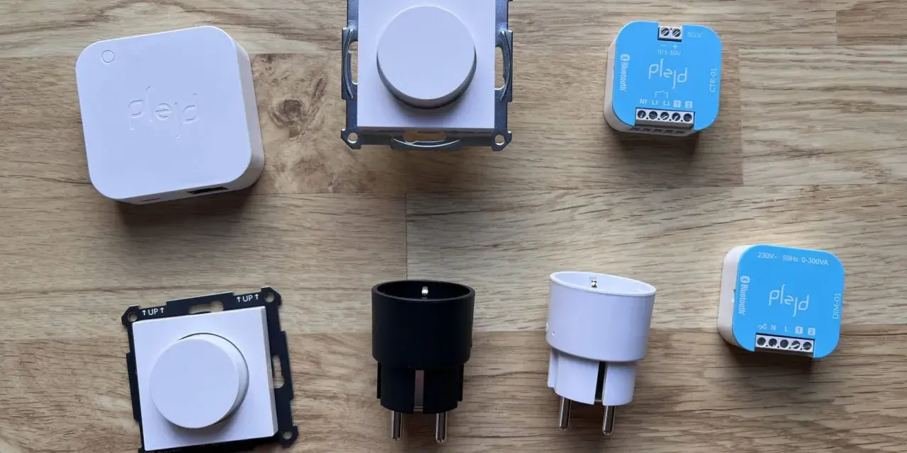 En samling Plejd-produkter, inklusive en vit Plejd-box, två dimmerknappar, två elkontakter och två styrenheter som stöder Plejd-protokoll.