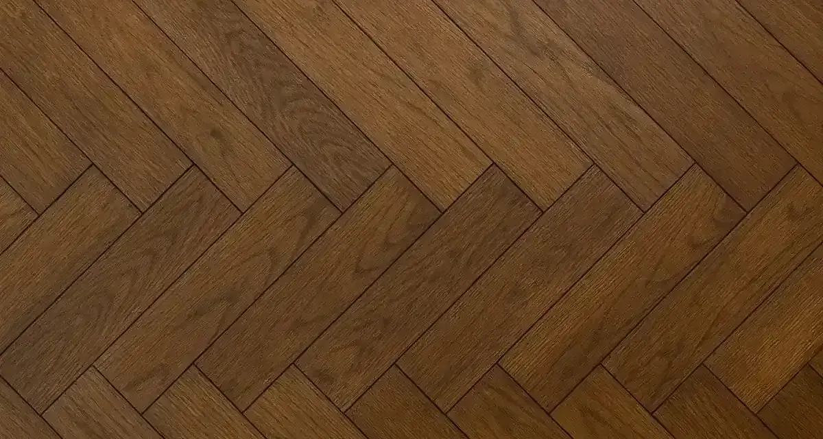 Vacker fiskbensparkett i mörkt trä, redo att slipa för att återfå sin glans.