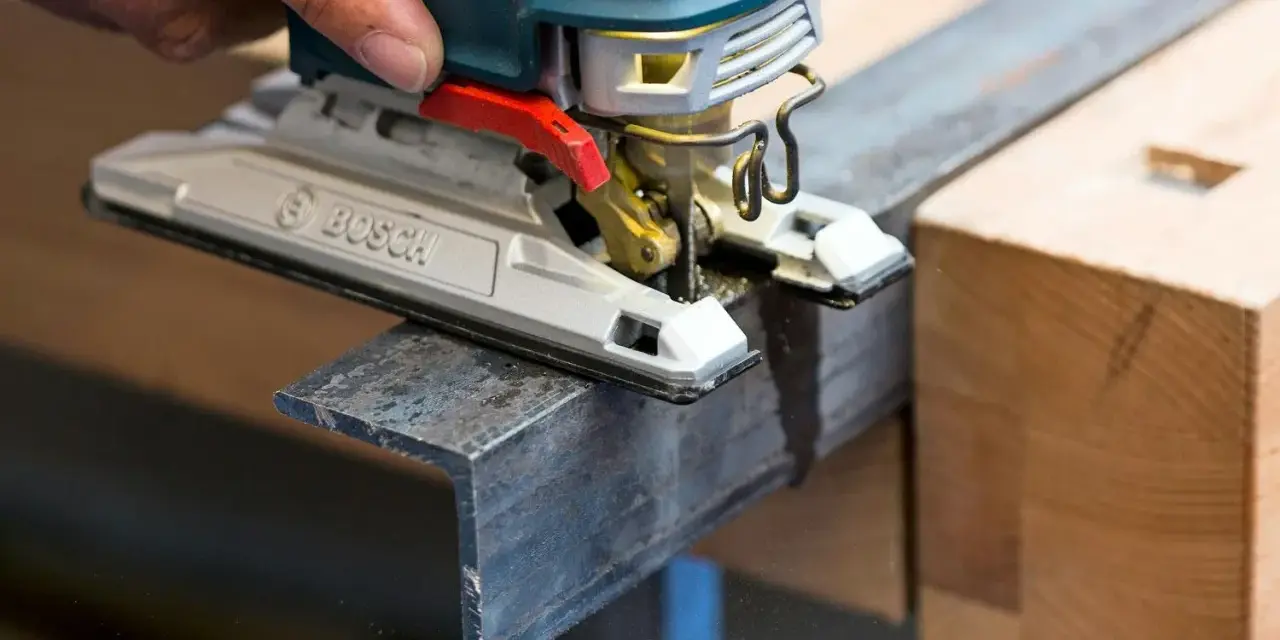 En hand använder en sticksåg för att såga snett i en metallprofil.