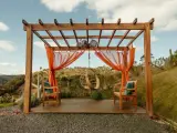 En vacker träpergola med orange draperier och hängstol. Perfekt för att bygga pergola på altan och njuta av utsikten.