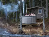 Fyra vänner njuter av en badtunna vid en sjö. Röken stiger från skorstenen, en mysig stund att bygga badtunna för.