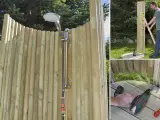 Man bygger en utedusch med trästolpar och en duschslang. Verktyg och material syns i bild.