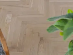 Ett nyslipat parkettgolv i fiskbensmönster, redo att skyddas. En grön växt och en del av en stol syns i bild.