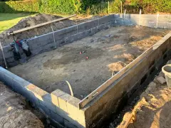 Byggarbetsplats med ett mura grund av betongblock. Schakt, spade och vattenpass syns.