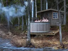 Fyra vänner njuter av en badtunna vid en sjö. Röken stiger från skorstenen, en mysig stund att bygga badtunna för.