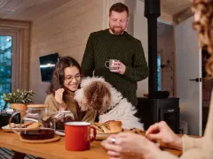 Familj med hund myser vid bordet med fika. Trots att det är lite dålig luft hemma, sprider sig värme och glädje.