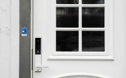 Vit ytterdörr med digitalt lås, låsklass 3, och en skylt för larm med åtgärd.