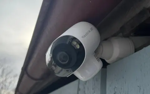 En vit Reolink Argus 4K övervakningskamera monterad under ett takutsprång.